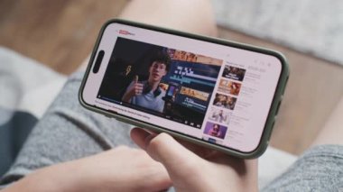 Akıllı telefon ekranında görüntülenen video düzenleme hakkında blog içerikli video paylaşım platformu. Kanepede otururken, cep telefonuyla film yapımı hakkında eğitici videolar izleyen gençlere yakın çekim.