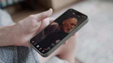 Ergenlerin, evdeki kanepede otururken cep telefonlarını kullanarak video içeriklerini izlemelerine yakın çekim yapın. Telefon ekranında kısa videolar gösterilen sosyal ağ beslemeli akıllı telefon uygulaması.