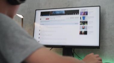 PC monitörü video paylaşım platformunu film yapımcılığıyla ilgili içerikle gösteriyor. Kulaklıklı beyaz çocuk evdeki kişisel bilgisayarda film ya da video düzenleme hakkında eğitim bloğu izliyor..