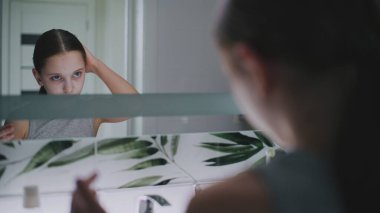 Güzel ergen sabahları lavabonun önünde duruyor ve saçlarını şekillendiriyor. Çekici genç kız banyoda aynaya bakıyor, saç stili yapıyor. Sabah banyosu rutini. Yaşam tarzı kavramı. Kapat..