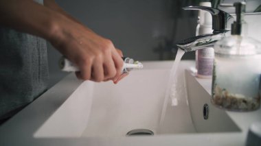 Beyaz çocuk banyoda aynaya bakar, dişlerini fırçalar. Ergen lavabonun önünde duruyor ve yatmadan önce elektrikli diş fırçası kullanıyor. Akşam banyosu rutini. Yaşam tarzı konsepti. Düşük açılı çekim.