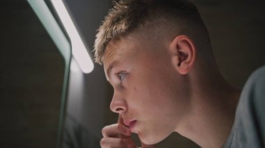 Beyaz çocuk banyoda dikiliyor ve aynadaki yansımasına bakıyor. Ergen, lavabonun yanında duruyor ve sabahları saç stili yapıyor. Tuvalet rutin konsepti. Yaşam tarzı. Arkadan bak. Kapat.