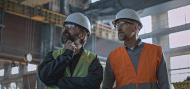 Güvenlik üniformalı iki profesyonel ağır endüstri mühendisi ve sert şapkalar imalat fabrikasında çalışma sürecini tartışıyor. Olgun yönetici, fabrika ya da atölyede çalışan yetişkin işçilerle konuşur. Yavaş çekim.