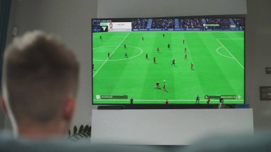 ZAPORIZHYA, UKRAINE - 7 Haziran 2024: TV ekranında gösterilen çevrimiçi futbol oyunu. Oturma odasında kanepede oturup boş zamanlarını geçirirken beyaz tenli bir çocuğun konsol oynaması..