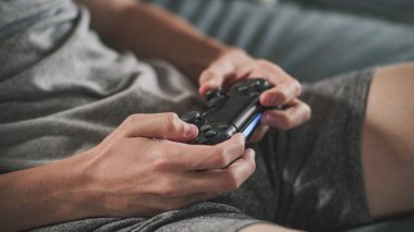 Oturma odasındaki kanepede oturan, kablosuz kumandayı kullanarak internet üzerinden oyun oynayan beyaz çocuğun ellerini kapat. Ergen dinleniyor ve hafta sonunu evde geçiriyor. Yaşam tarzı kavramı.