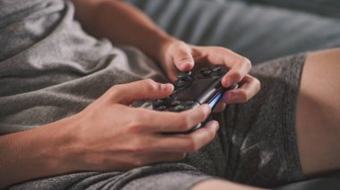 Oturma odasındaki kanepede oturan, kablosuz kumandayı kullanarak internet üzerinden oyun oynayan beyaz çocuğun ellerini kapat. Ergen dinleniyor ve hafta sonunu evde geçiriyor. Yaşam tarzı kavramı.