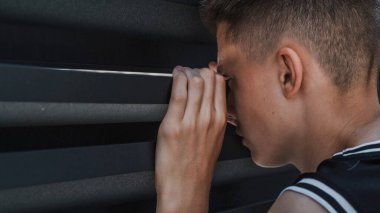 Slow motion of serious and concentrated Caucasian teenager peeking and carefully looking through gap between the iron fence while standing in the courtyard of the house. Lifestyle concept. Close Up. clipart