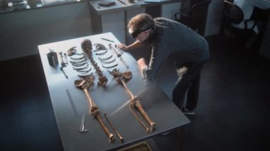 Modern arkeoloji laboratuvarı: VR kulaklıklı olgun arkeologun yüksek açısı, gelişmiş gerçeklik teknolojisi kullanılarak soyu tükenmiş antik bir insanın iskelet kalıntılarını inceliyor. Bilim adamı tarihi araştırmalar yapıyor..