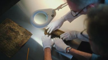 Bilim adamları soyu tükenmiş insan medeniyetinin kültürel mirasını inceliyor ve keşfediyorlar. Eldivenli iki arkeolog, antik Mısır papirüsünü dikkatlice arkeoloji laboratuarındaki masada açtılar. Arkeoloji.