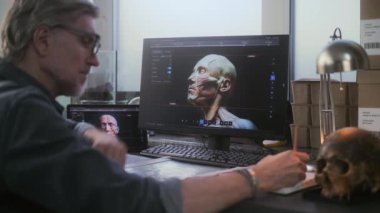 Olgun arkeolog fosil kafatasını inceliyor, tablet bilgisayar ve bilgisayar kullanıyor ve soyu tükenmiş eski insan kafasının 3 boyutlu modelini oluşturuyor, defterine notlar yazıyor. Bilim adamı modern arkeoloji laboratuvarında çalışıyor.