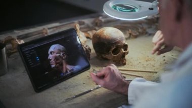 Arkeologlar lambanın altında fosil kafatası incelerler, tablet bilgisayarda gösterilen görselleştirme teknolojisiyle yaratılan antik insan kafasının 3 boyutlu modelini tartışırlar. Bilim adamları modern arkeoloji laboratuvarında çalışıyorlar..