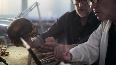 İki bilimadamı nesli tükenmiş insan kalıntılarını analiz ediyor, dijital tablet bilgisayar kullanarak fosil kafatası üzerinde tarihi ve bilimsel araştırmalar yapıyorlar. Arkeologlar modern arkeoloji laboratuvarında çalışıyorlar..