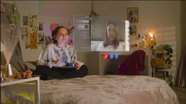 Genç kız tablet bilgisayar kullanıyor AR sohbet uygulamasındaki arkadaşıyla sanal gerçeklik kullanarak konuşuyor, evde yatakta oturuyor. VFX holografik video arayüzü grafikleri. Fütürist metaevren. Artırılmış gerçeklik