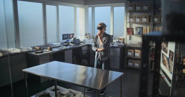 AR kulaklığı takan olgun bir arkeolog veya bilim adamı, sanal gerçeklik teknolojisi kullanılarak arkeoloji laboratuvarında tarihi ve bilimsel bir araştırma yürütüyor. İş arkadaşı arka planda PC üzerinde çalışır.