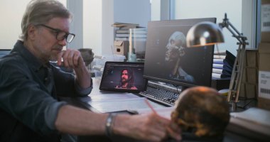 Olgun bilim adamı ya da araştırmacı fosil kafatası üzerinde çalışıyor, eski nesli tükenmiş insan kafasının 3 boyutlu görselleştirilmiş tablet ve bilgisayarını kullanıyor, defterine notlar yazıyor. Arkeolog arkeoloji laboratuvarında çalışıyor..