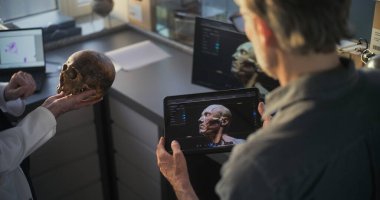 İki arkeolog fosil kafatası üzerinde çalışıyor, görselleştirme teknolojisini kullanarak tarih öncesi soyu tükenmiş insan kafasının 3 boyutlu modelini tablet ve bilgisayarda yaratıyorlar. Bilim adamları tartışıyor, arkeoloji laboratuvarında çalışıyorlar..