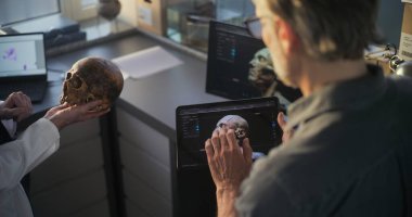 İki arkeolog fosil kafatası üzerinde çalışıyor, görselleştirme teknolojisini kullanarak tarih öncesi soyu tükenmiş insan kafasının 3 boyutlu modelini tablet ve bilgisayarda yaratıyorlar. Bilim adamları tartışıyor, arkeoloji laboratuvarında çalışıyorlar..