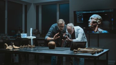 Modern arkeoloji laboratuvarı: İki arkeolog veya bilim adamı, tarih öncesi insan iskeletinin profesyonel kamerayla çekilmiş fosil örneklerini tripodun üzerinde tartışıyor. Arkeoloji kavramı