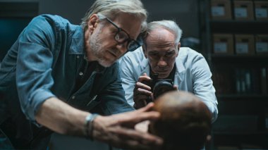 Modern arkeoloji laboratuvarı: İki arkeolog fosil kalıntılarını fotoğraflamak için profesyonel kamera kurdular ve tartıştılar. Laboratuvar önlüklü kıdemli bilim adamı flaşla fotoğraf çekiyor. Arkeoloji kavramı.