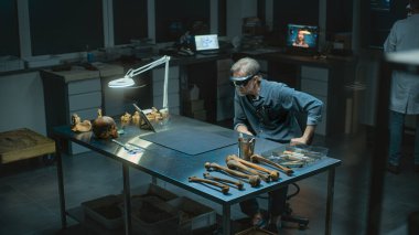 Geceleyin arkeoloji laboratuvarı: AR 'daki olgun arkeolog veya bilim adamı, sanal gerçeklik ve tablet bilgisayar kullanarak antik insan kalıntıları üzerinde tarihi araştırmalar yürütüyor. Yüksek açı