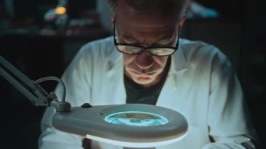 Bilim adamı geceleri arkeoloji laboratuvarında çalışıyor. Kıdemli arkeolog, fosil kemiğin ölçümlerini profesyonel ölçüm araçları kullanarak alıyor, büyüteç altında tarih öncesi insan kalıntıları üzerinde çalışıyor..