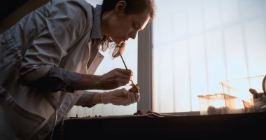 Kadın bilim adamı veya arkeolog kemikleri fırçayla temizliyor, tarih öncesi insan veya yırtıcı iskelet kalıntıları üzerinde çalışıyor. Gelişmiş arkeoloji laboratuvarında fosil koleksiyonu. Gün batımı ışığı. Yavaş Hareket.