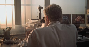 Olgun kimyager ya da mikrobiyolog fosil örneğini mikroskop altında analiz eder. Bilim adamı veya arkeolog ileri arkeoloji laboratuvarında profesyonel ekipmanlarla çalışıyor. Gün batımı ışığı.