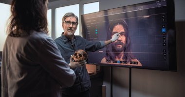 Erkek ve kadın bilim adamları veya arkeologlar konuşurlar, fosil kafatasını incelerler ve ileri arkeoloji laboratuvarında bilimsel araştırmalar yaparlar. Eski insanın 3 boyutlu görüntüsü büyük ekranda görüntülendi.