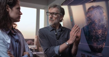 Erkek ve kadın arkeologlar kültürel antikaları tartışıyor ve inceliyor, gelişmiş arkeoloji laboratuvarlarında tarihi araştırmalar yapıyorlar. Büyük ekranda gösterilen antik kil vazonun 3 boyutlu görüntüsü.