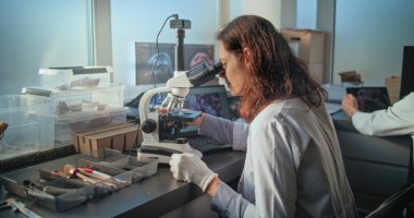 Kadın kimyager ya da mikrobiyolog mikroskop altında fosil analizi yapar. Eski insan iskeletinin kemikleri ve masada duran aletler. Bilim adamları gelişmiş ve donanımlı arkeoloji laboratuvarında çalışıyorlar..