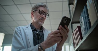 Yetişkin bilim adamlarının sohbetlerine yakın olmak, cep telefonuyla internette sörf yapmak, bilimsel araştırmalar için yapay zeka sohbet robotunu kullanmak, klasörlerin yanında durmak. Arkeoloji bilim laboratuvarı. Düşük Açı.