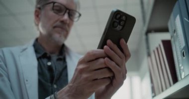 Laboratuvar önlüğü giymiş yetişkin bir bilim adamının sohbet ederken, internette veya cep telefonuyla sosyal medyada sörf yaparken yakın plan çekimleri. Modern arkeoloji laboratuvarı. Düşük Açı