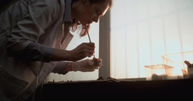 Kadın bilim adamı veya arkeolog kemikleri fırçayla temizliyor, tarih öncesi insan veya yırtıcı iskelet kalıntıları üzerinde çalışıyor. Gelişmiş arkeoloji laboratuvarında fosil koleksiyonu. Gün batımı ışığı. Yavaş Hareket.