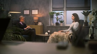 Olgun psikolog kadın hastalarla konuşur, psikoterapi sağlar. Yetişkin bir kadın sandalyede oturur terapi seansı sırasında terapistle sorunları tartışır. Golden Retriever köpeği. Ruh Sağlığı.