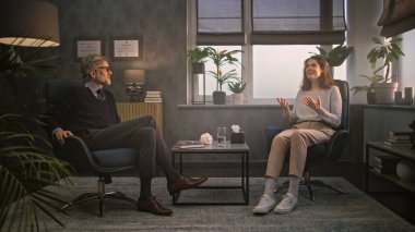 Kadın sandalyede oturuyor, konuşuyor ve terapi seansında psikologla olumlu duyguları paylaşıyor. Olgun profesyonel terapist kadın hastaları dinler, psikoterapi sağlar. Psikoloji.