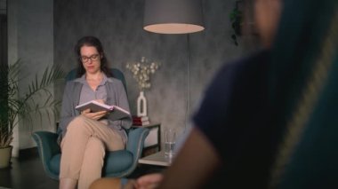 Kadın psikolog not defterine not alır, hastayı dinler, iletişim kurar ve sorular sorar. Terapist terapi seansı sırasında psikoterapi sağlar. Duygusal destek ve psikolojik yardım.