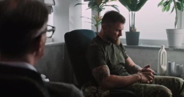 Travma sonrası stres bozukluğu olan bir asker, psikoterapist ya da psikologla terapi seansı sırasında sandalyeye oturur, ağlar ve olumsuz duygular yaşar. Travma sonrası stres bozukluğu. Omzunun üstünden..