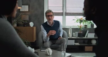 Mutlu psikoterapist genç aileyle konuşur, danışmanlık seansı sağlar. Çok ırklı çiftlerin arka planda el ele tutuşup çiftler terapisi üzerine tartıştıktan sonra kahkahalarla gülmeleri..