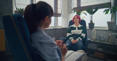 Elinde not defteri olan kadın terapistin arka planda oturup ergenlere terapi uygulaması. Pembe saçlı genç kız duygularını paylaşıyor, terapi seansında psikologla sorunları tartışıyor..