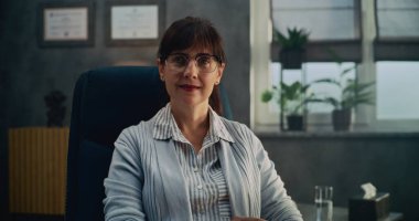 Gözlüklü kadın terapistin portresi sandalyede oturuyor, gülümsüyor ve kameraya bakıyor. Profesyonel psikolog psikoloji bürosunda çalışıyor. Psikoterapistle terapi seansı. Ruh Sağlığı.