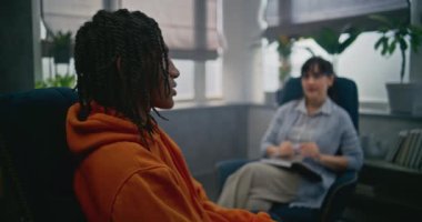 Afrikalı Amerikalı çocukla psikoterapist buluşması. Psikolog sandalyeye oturur, genç hastaları dinler. Genç çocuk kadın terapistle konuşuyor, aile sorunlarını tartışıyor. Psikoloji konsepti.