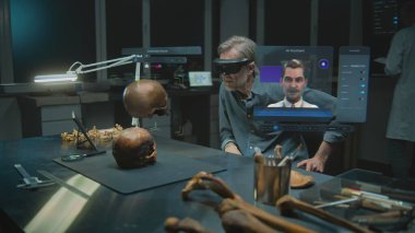 Gelişmiş arkeoloji laboratuvarı: VR kulaklık alanında arkeolog fosil kafatası kullanarak artırılmış gerçeklik üzerinde bilimsel araştırmalar yürütüyor. Yapay zeka asistanı ve web tarayıcısıyla sanal ekranın 3 boyutlu animasyonu. VFX