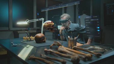 Gelişmiş arkeoloji laboratuvarı: VR kulaklık alanında arkeolog fosil kafatası kullanarak eski insan anatomisini artırılmış gerçeklikte inceliyor. Tarama yazılımının kullanıcı arayüzü ile üç boyutlu görüntüleme.