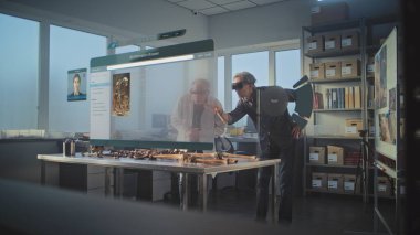 Gelişmiş arkeoloji laboratuvarı: VR kulaklıklarındaki iki arkeolog artırılmış gerçekliği kullanarak antik insan iskeletini inceliyor. Yapay zeka asistanı ve bilgi web tarayıcısıyla üç boyutlu holografik görüntü grafikleri.