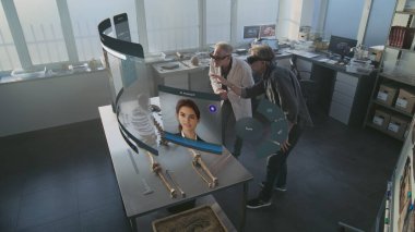 Gelişmiş arkeoloji laboratuvarı: VR kulaklıklarda çalışan iki arkeolog iskelet üzerinde çalışmalar yapıyor ve geliştirilmiş gerçeklik kullanıyor. Yapay zeka ses asistanı ve bilgi web tarayıcısıyla üç boyutlu sanal görüntü canlandırması.