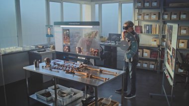 Gelişmiş arkeoloji laboratuvarı: VR kulaklıklarındaki iki arkeolog, artırılmış gerçeklik kullanılarak antik iskelet üzerinde tarihi araştırmalar yürütüyor. Yapay zeka asistanı ve web tarayıcısıyla sanal görüntünün 3 boyutlu grafikleri