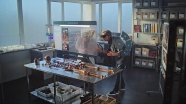 Gelişmiş arkeoloji laboratuvarı: VR kulaklıklarındaki iki arkeolog, artırılmış gerçeklik kullanılarak antik iskelet üzerinde tarihi araştırmalar yürütüyor. Yapay zeka asistanı ve web tarayıcısıyla sanal görüntünün 3 boyutlu grafikleri