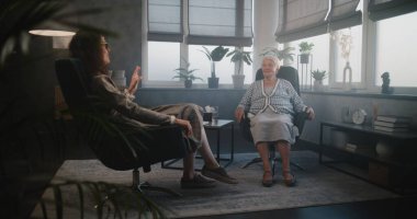 Kadın psikoterapist ve yaşlı hasta toplantıda gülüyor, akıl hastalığının tedavisinde kaydedilen ilerlemeyi tartışıyorlar. Terapistle seansta olumlu duygular. Yaşlılara psikolojik yardım.