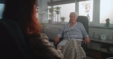 Kadın psikoterapist yaşlı bir hastaya depresyon tedavisi uyguluyor. Terapist ve hasta konuşması. Kadın müvekkil karşı psikolog koltuğunda oturuyor ve zihinsel sorunlarla ilgili soruları cevaplıyor..