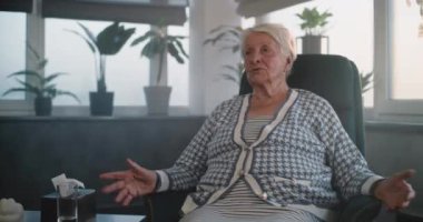 Kadın hasta oturur ve psikoterapistle konuşur. Yaşlı kadın psikolojik travmayı tartışıyor, terapi seansı sırasında çözümler buluyor. Kadın psikolog not alır, hastayı dinler..
